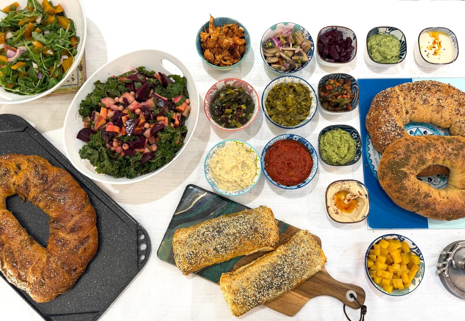 Shabbat table laid out with two challahs, beef roulade, a row of salatim and fresh salads
